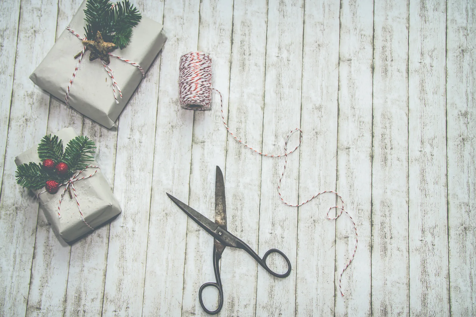 Wrapped gifts on a whitewashed table with twine, scissors and sprigs of greenery