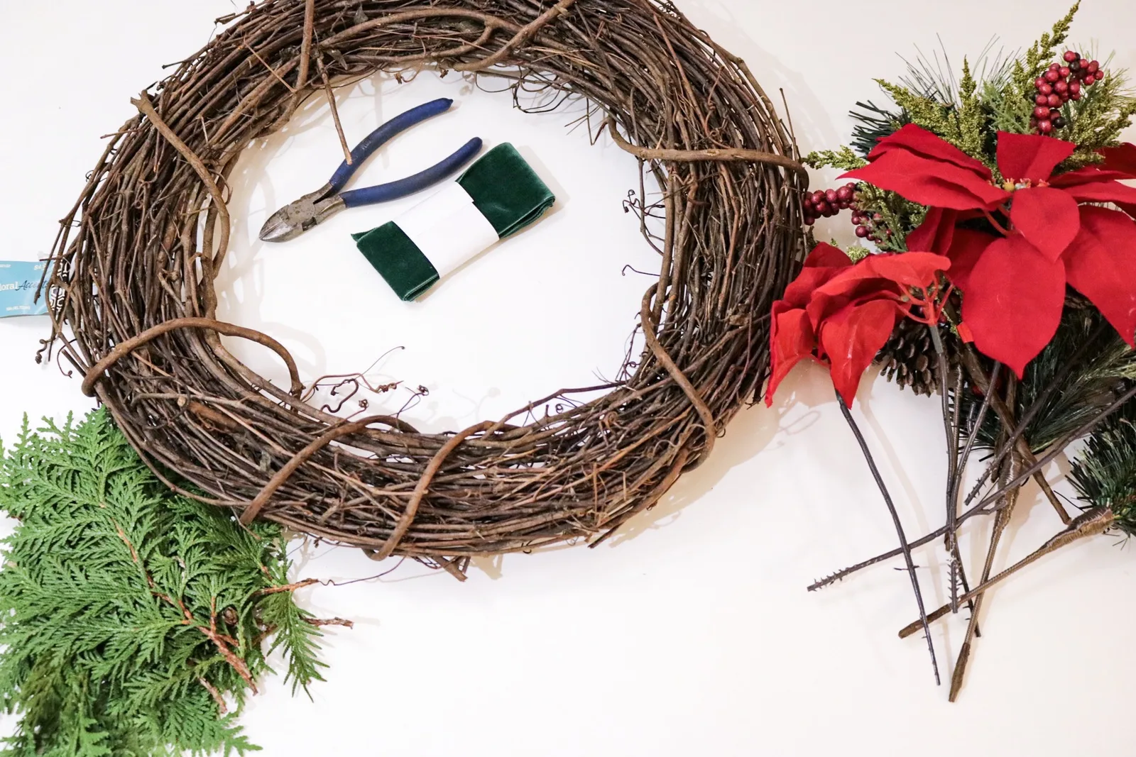 Double sided Christmas wreath on a vine base with red poinsettias, pine picks and holly berries, hanging in a window