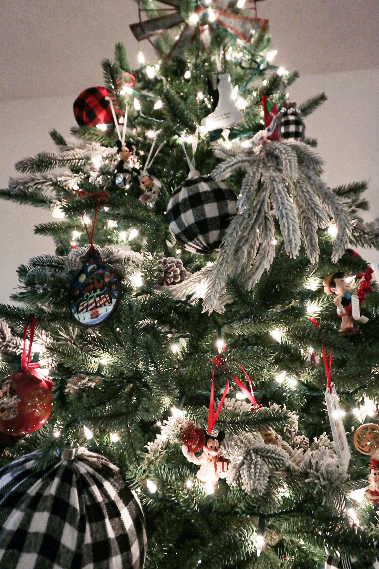 A fully lit Christmas tree decorated with buffalo check baubles and frosted white picks