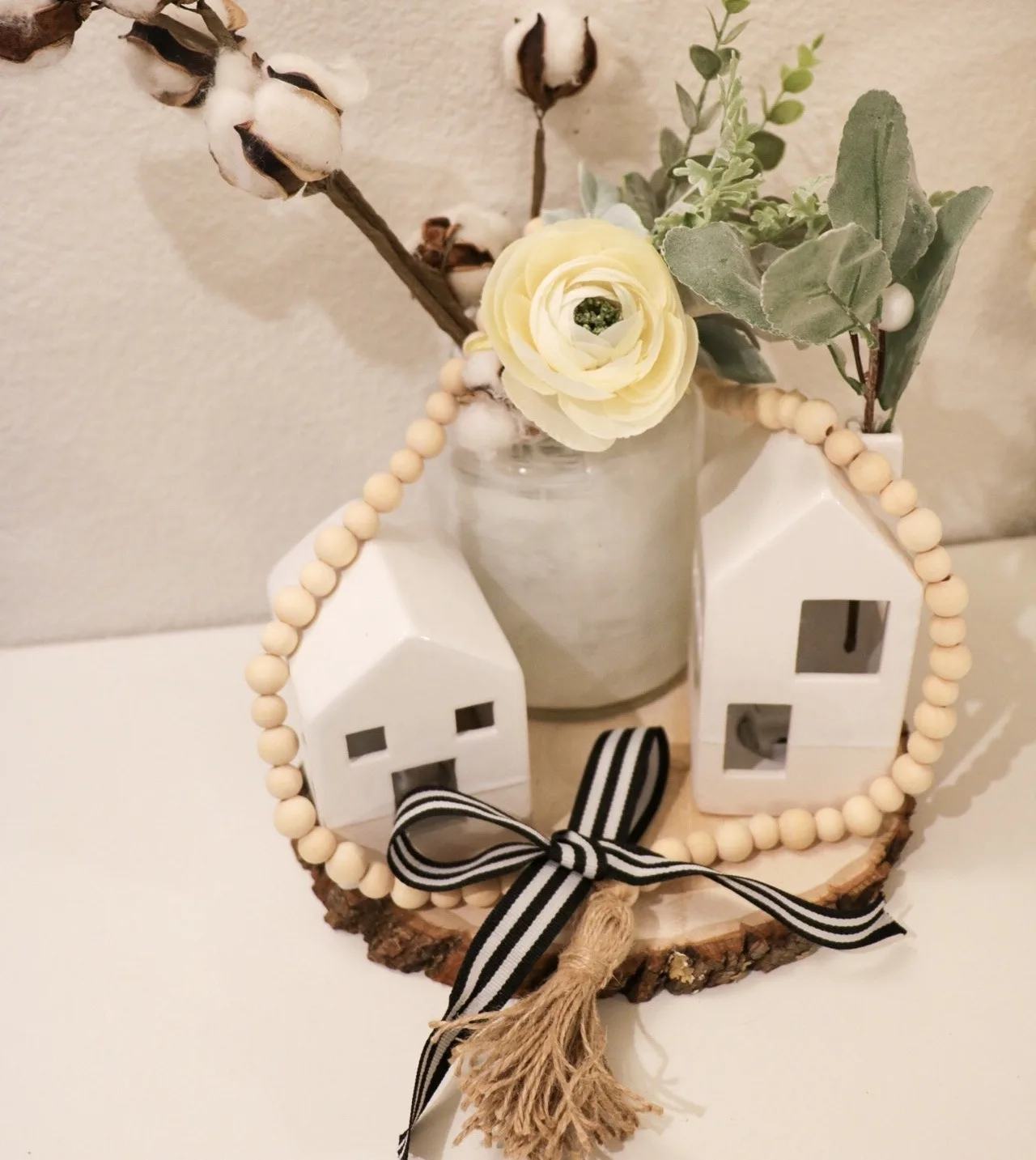 A neutral winter vignette — small white ceramic houses, cotton stems, eucalyptus and a wooden bead garland